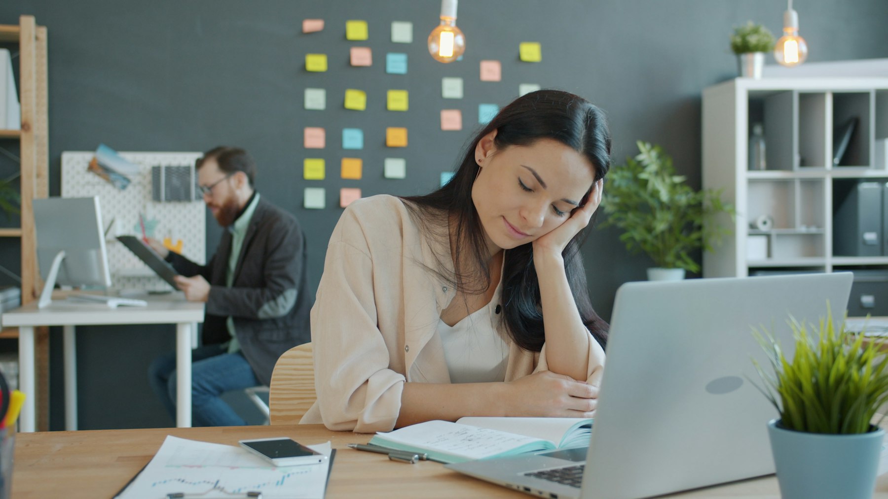 Femme fatiguée assise à son bureau, la tête appuyée sur la main en fin de journée