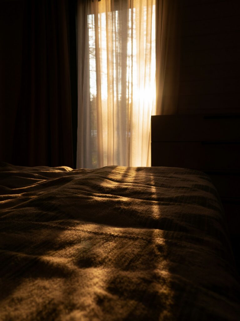 Lumière du soir filtrant à travers les rideaux d'une chambre et tombant sur le lit