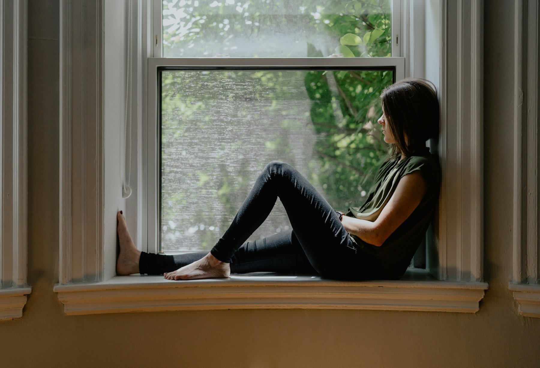 Femme assise sur le rebord d'une fenêtre le matin, prenant le temps de respirer lentement