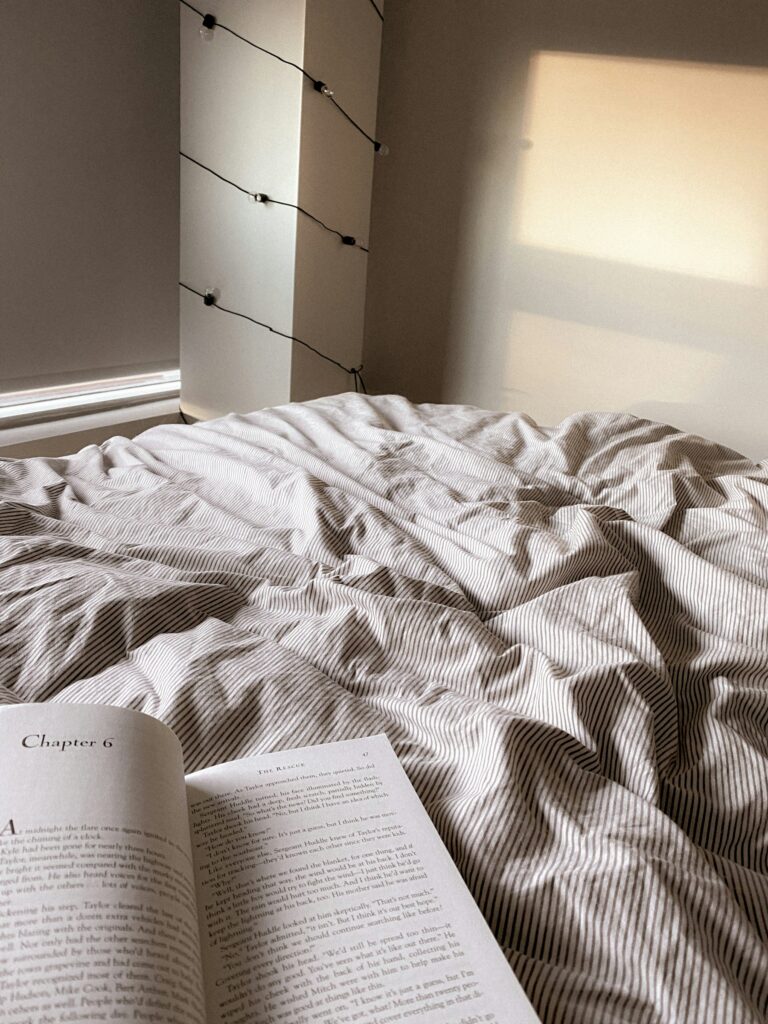 Livre papier ouvert posé sur les draps clairs d'un lit, à la place de l'écran