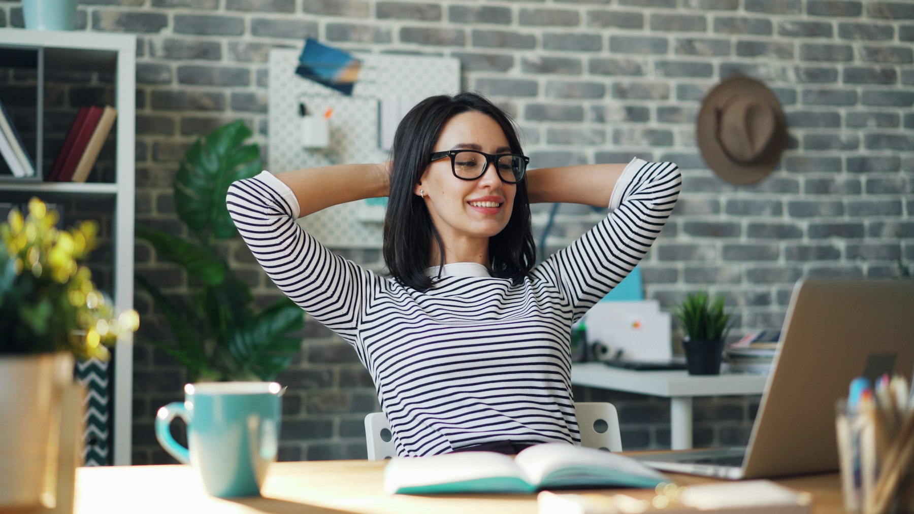 Femme assise à son bureau, mains derrière la tête, qui relâche ses épaules devant l'ordinateur