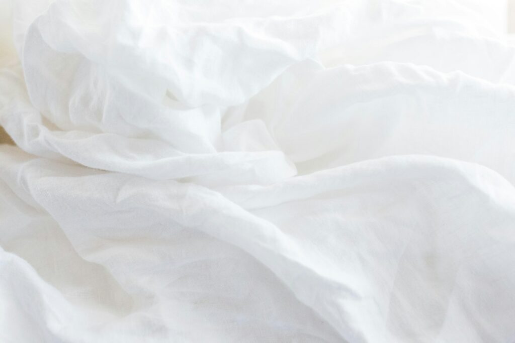 Gros plan sur un oreiller et des draps en lin blanc baignés de lumière douce