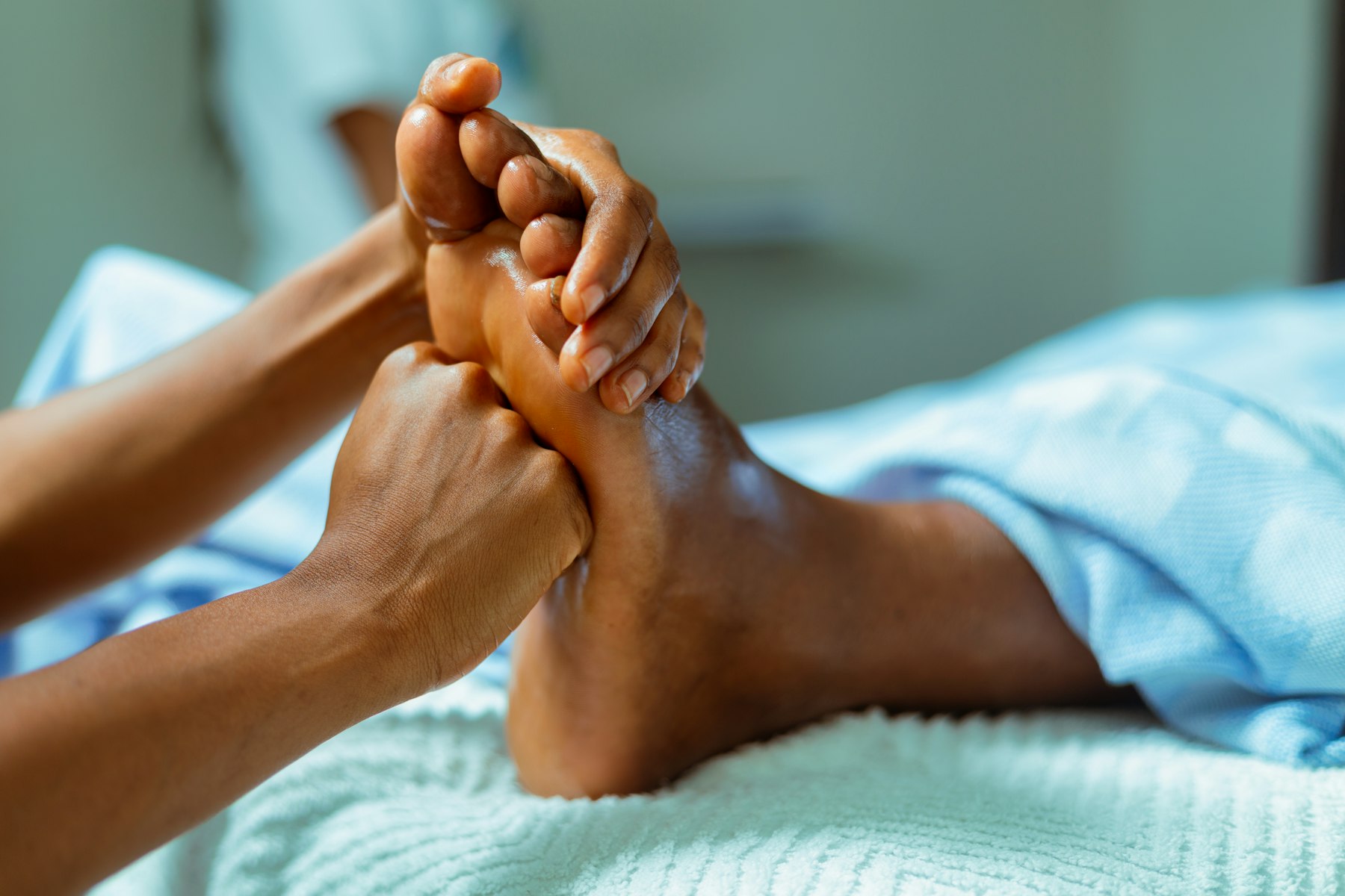 Mains de praticienne massant la plante d'un pied posé sur une serviette blanche
