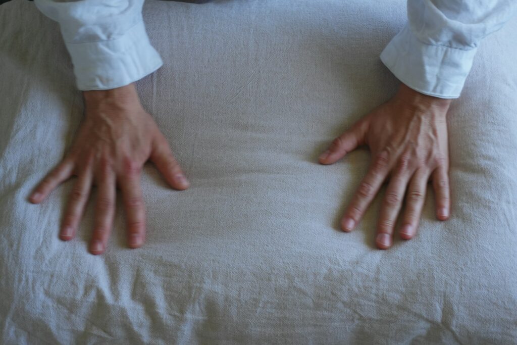 Mains relâchées posées sur un coussin en lin beige après une contraction musculaire