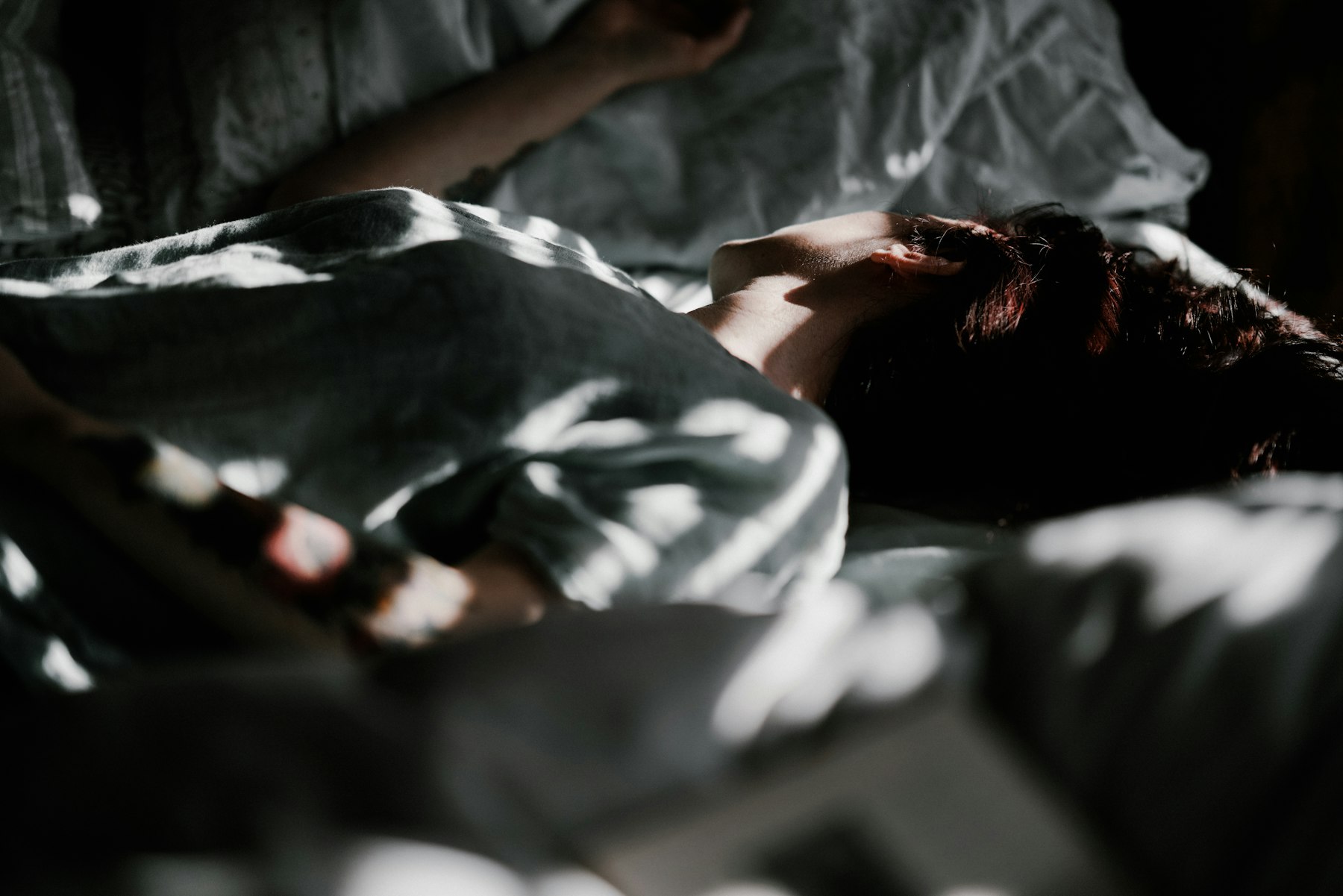 Personne allongée sous une couverture dans un lit en pénombre, en train de respirer calmement