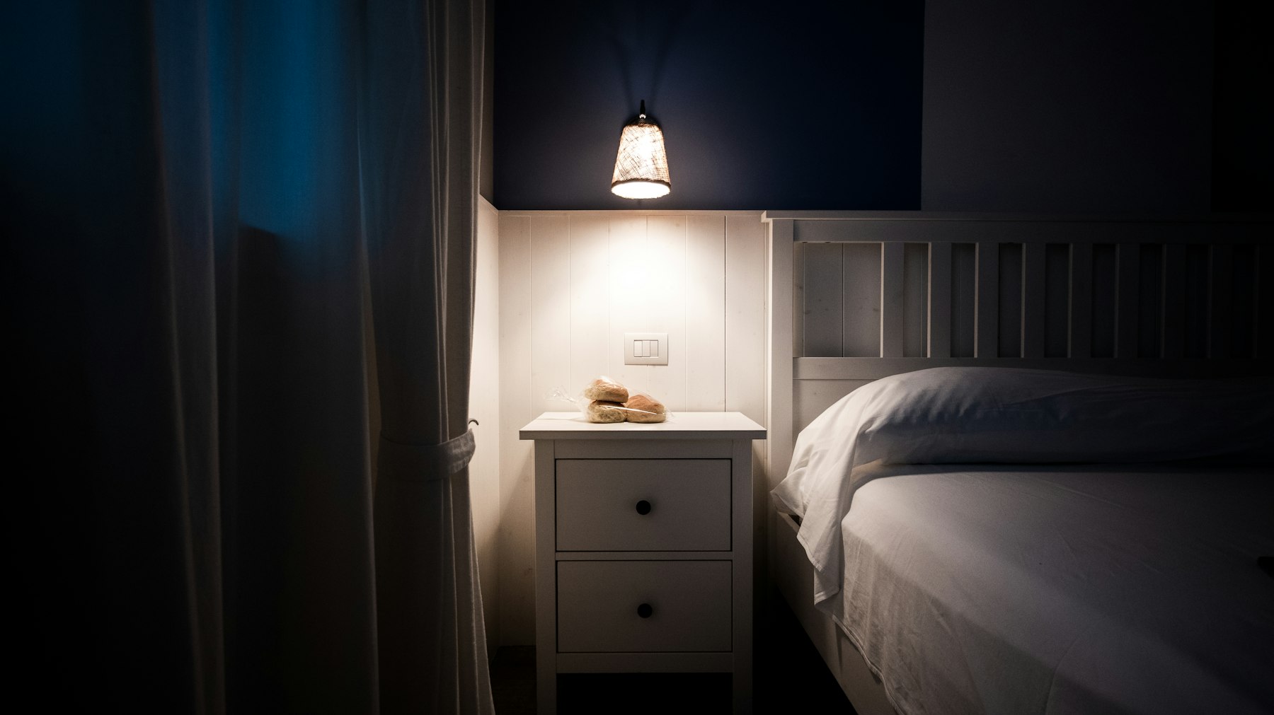 Lampe de chevet allumée sur une table de nuit, dans une chambre plongée dans la pénombre