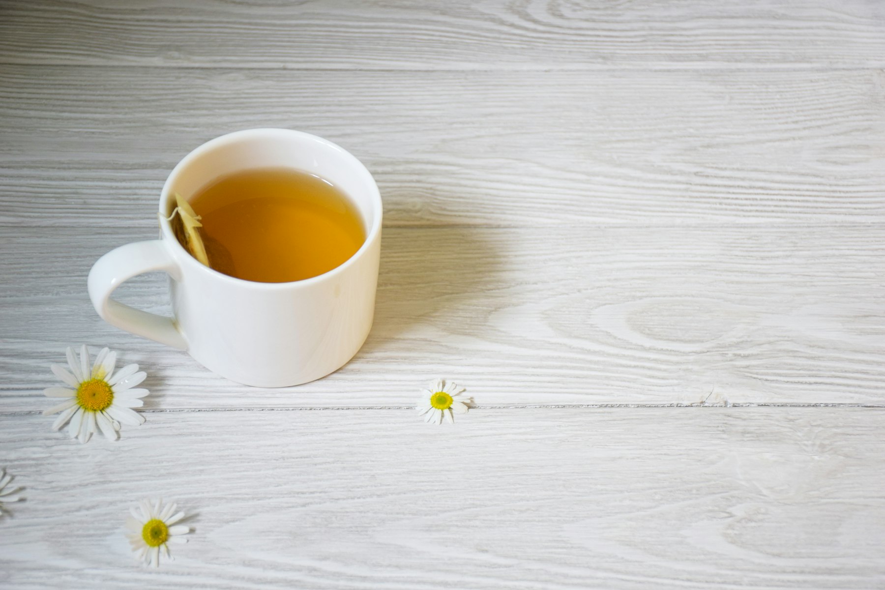 Tasse blanche de tisane de camomille posée sur une table en bois clair